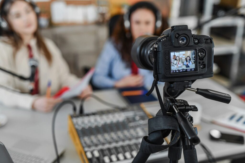 Podcast Recording With Camera On Tripod Capturing Two Women Interviewing And Laughing